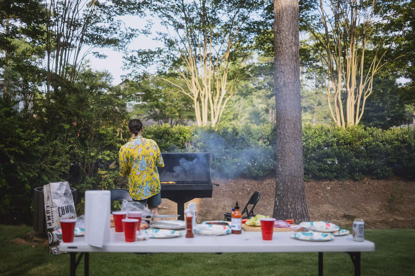 Someone grilling outdoors with a table of food and drinks in the foreground