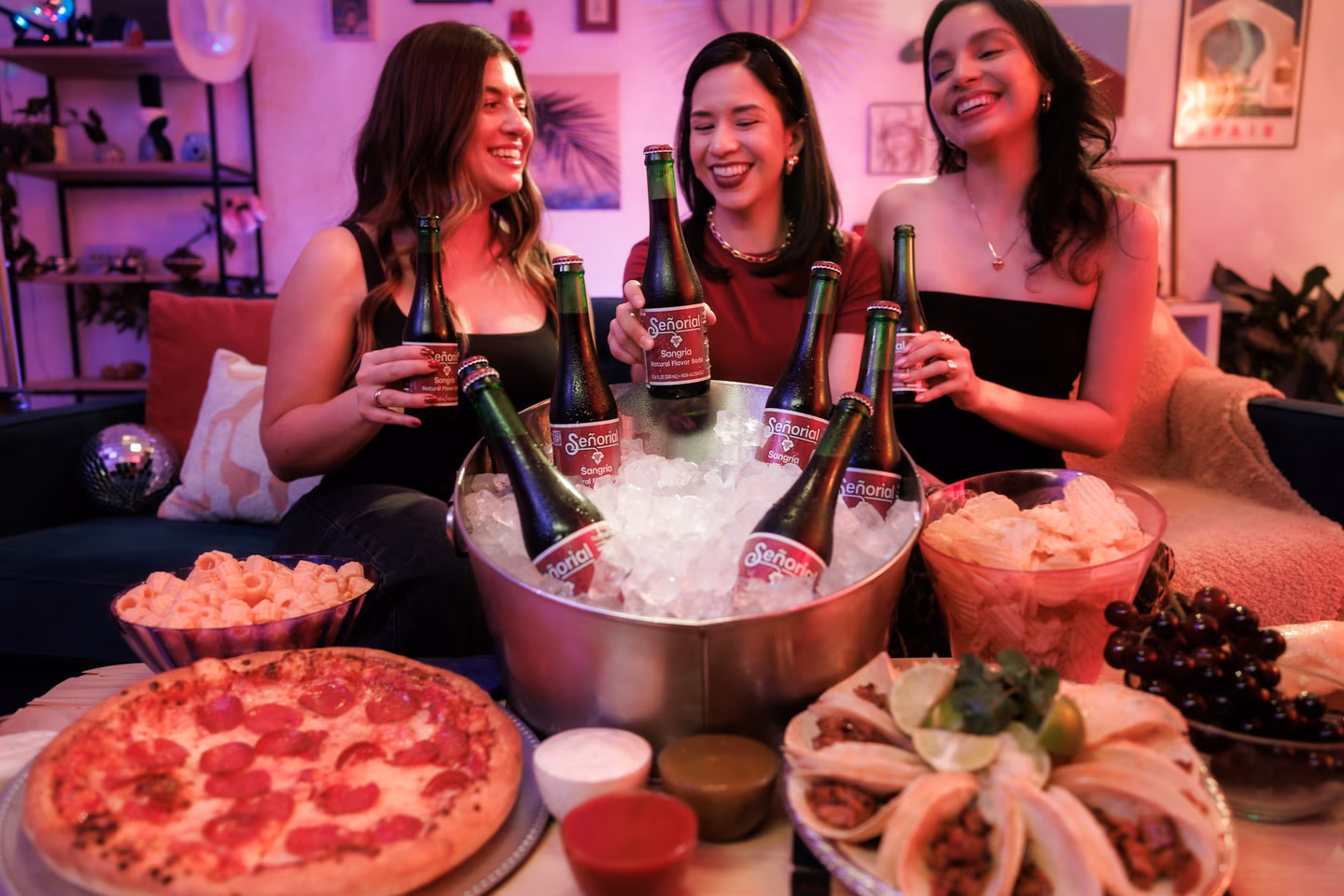 Three friends laughing over beer and snacks at a party